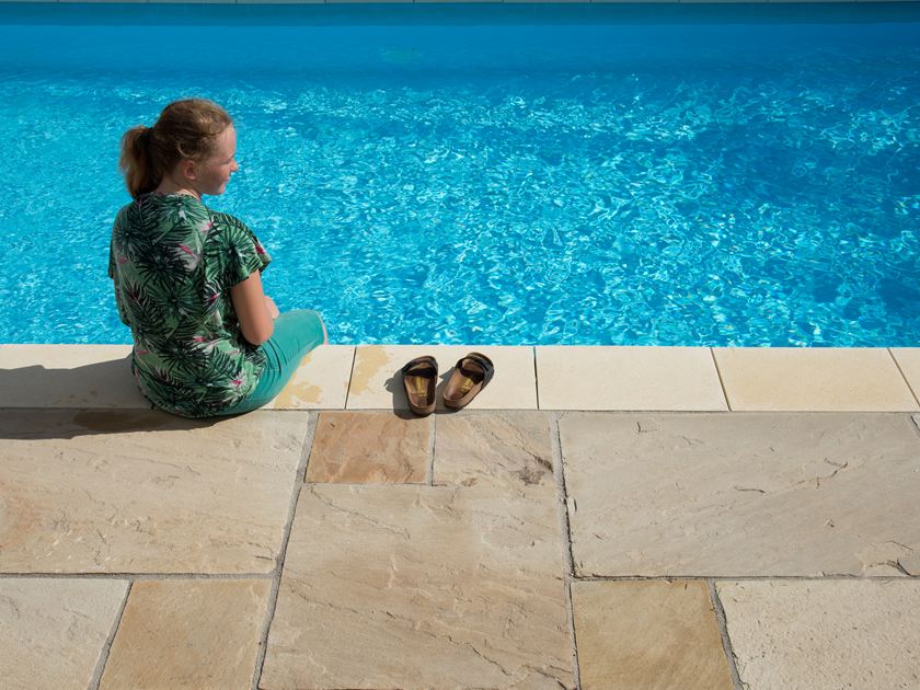 Meisje zittend bij blauw zwembad met zandstenen platen Gele munt