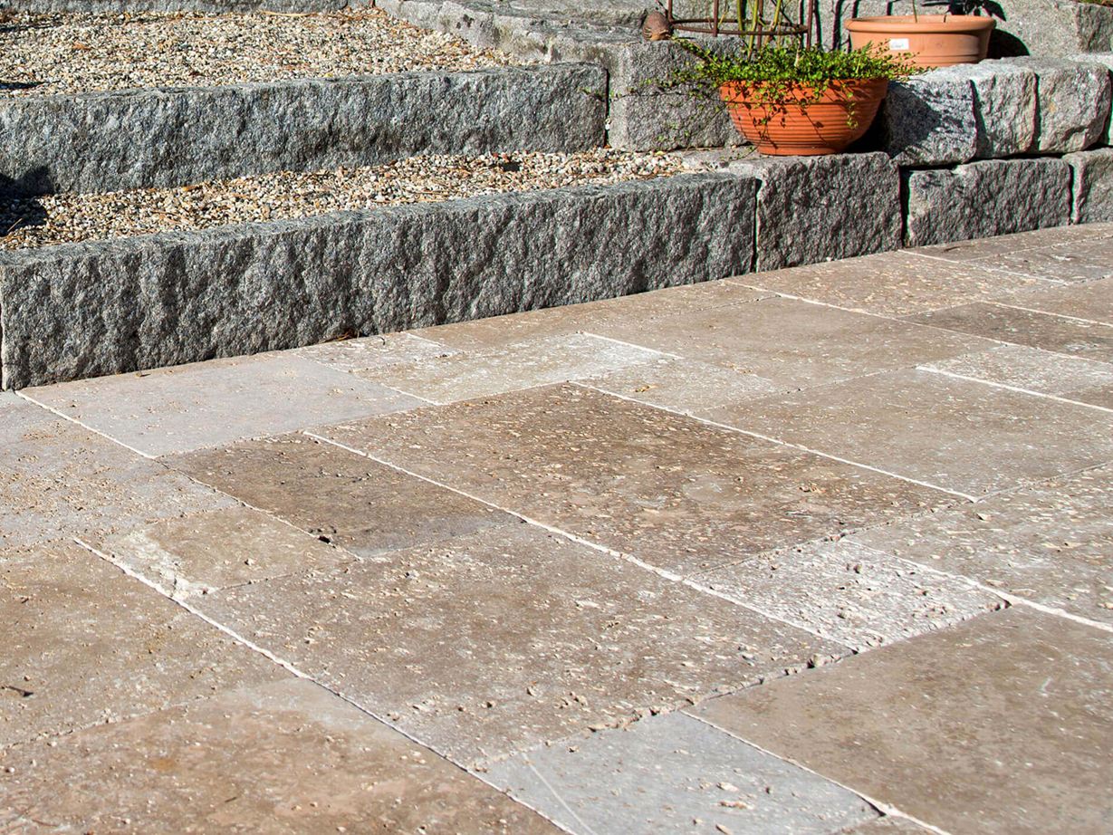 Terras met natuurstenen platen van bruin travertin, op de achtergrond een trap met granieten stenen