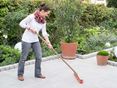 Een vrouw maakt een granieten terras schoon met een bezem, een natuurlijke tuin op de achtergrond