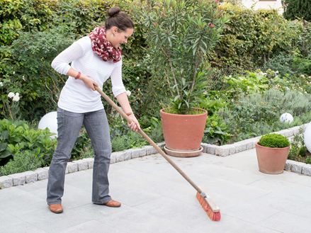 Een vrouw maakt een granieten terras schoon met een bezem, een natuurlijke tuin op de achtergrond