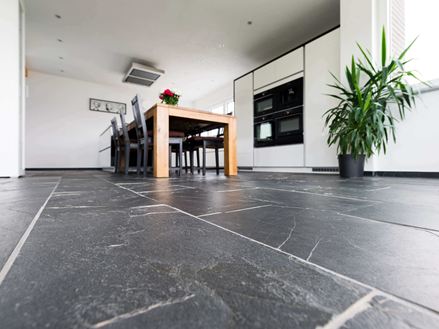 Kikkerperspectief op zwarte rustieke leistenen vloer met houten eettafel en plant op de achtergrond