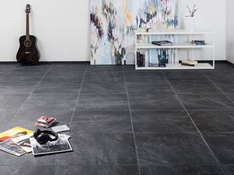 Moderne keramische tegels met leisteenlook in een woonkamer met een modern schilderij op de achtergrond en een gitaar aan de muur