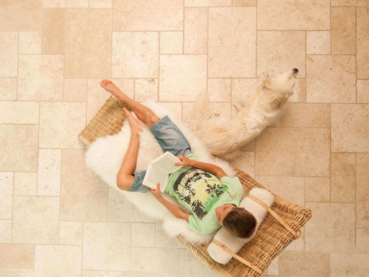 Lezende jongen in een ligstoel op lichte travertin tegels gelegd in Romeins verband