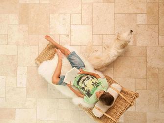 Lezende jongen in een ligstoel op lichte travertin tegels gelegd in Romeins verband