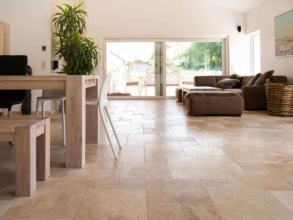 Woonkamer met bruine bank, witte muren en medium travertin tegels in bruin-beige als vloerbedekking