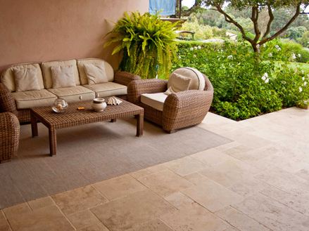 Entree van een mediterraan hotel met rieten fauteuils, travertin vloeren en een groene tuin op de achtergrond