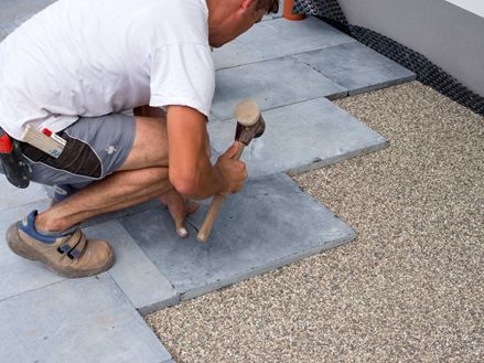 Hardstenen terrasplaten worden gelegd in een bed van hoogwaardige steenslag