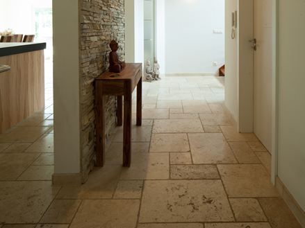 Gang met lichte travertin tegelvloer, kleine houten tafel en natuurstenen lambrisering op een muur