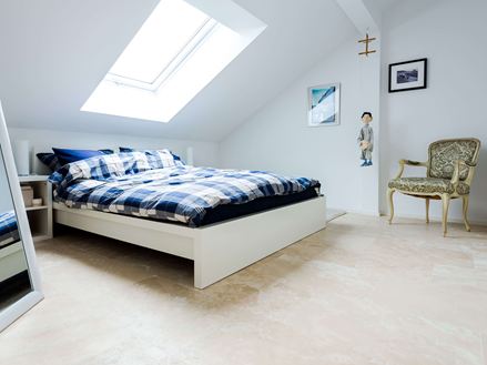 Een lichte slaapkamer onder het dak met Medium Line travertin tegels als vloerbedekking