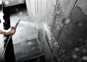 Hand houdt een douchekop tegen een muur met donkere stenen tegels