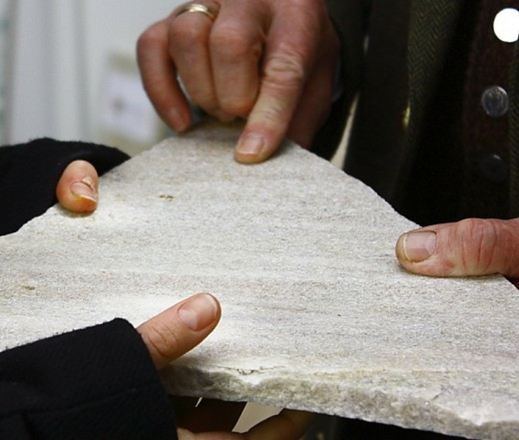 Twee handen houden een stuk natuursteen van Taunus kwartsiet vast