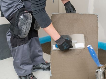 Een tegelzetter brengt lijm aan op de achterkant van een tegel