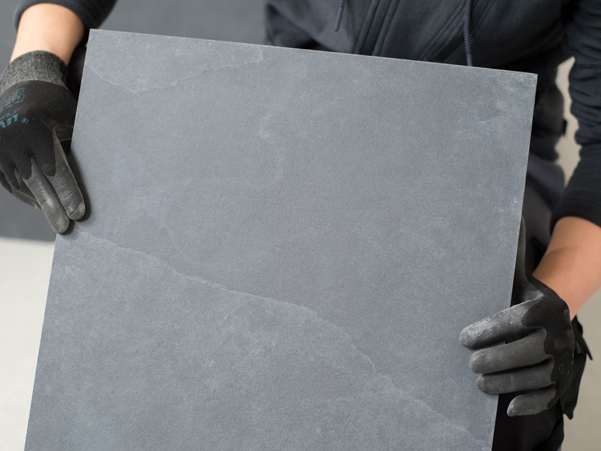 Tegelzetter houdt een leistenen tegel voor de camera