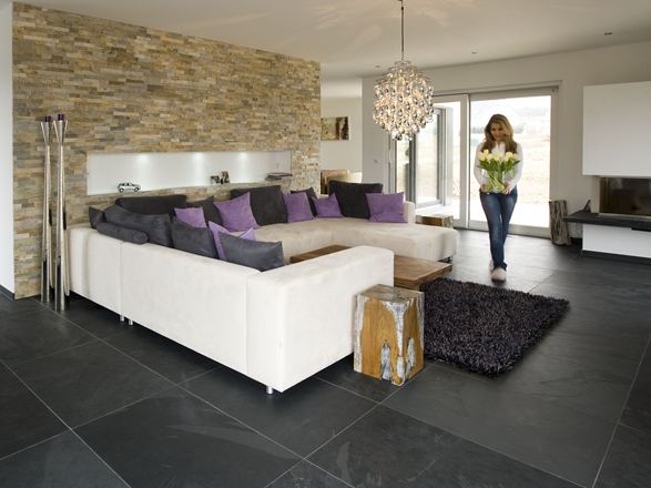 Moderne woonkamer met natuurstenen lambrisering aan de muur, leistenen tegels als vloer en een witte bank