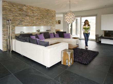 Moderne woonkamer met natuurstenen lambrisering aan de muur, leistenen tegels als vloer en een witte bank